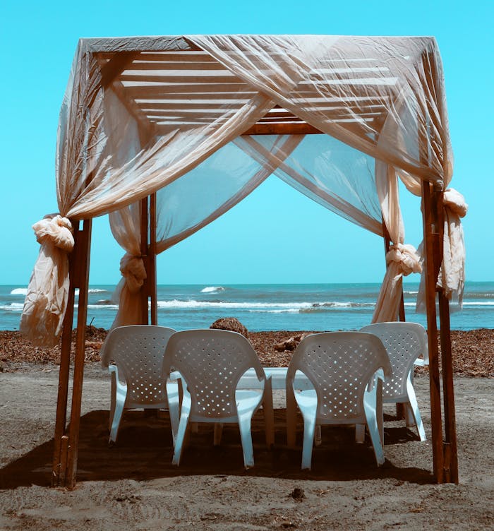 Relaxing gazebo setup on a sandy beach with ocean waves in the background. Perfect for leisure and vacation.