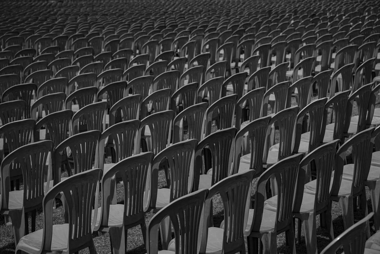 Black and white image of rows of empty plastic chairs creating a pattern.